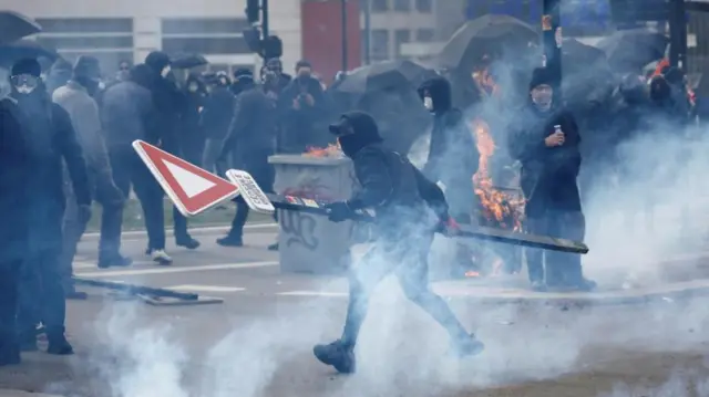 A masked protester holds a road sign amid tear gas during clashes at a demonstration as part of the tenth day of nationwide strikes and protests against French government's pension reform in Nantes, France, March 28, 2023.