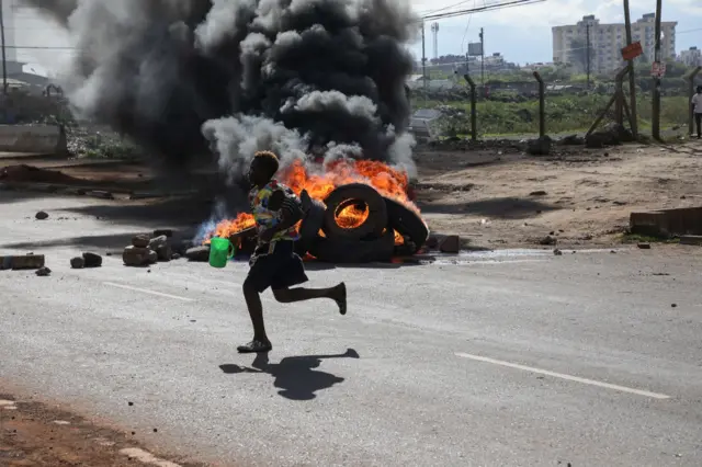 A protester runs past burning tires during a demonstration called by Azimio party leader Raila Odinga over the cost of living and president William Ruto's administration.