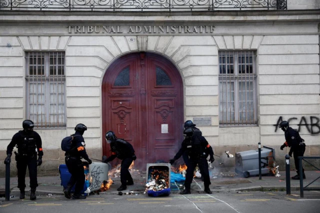 French police remove burning garbage bins in front of the entrance of the administrative court during clashes at a demonstration in Nantes, France