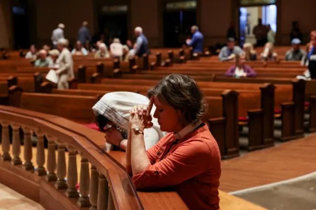 Two women pray at a vigil, one of them wearing a pastor's co