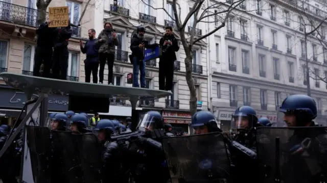 French riot police stand in position near a broken bus stop during clashes at a demonstration as part of the tenth day of nationwide strikes and protests against French government's pension reform, in Paris, France, March 28, 2023.