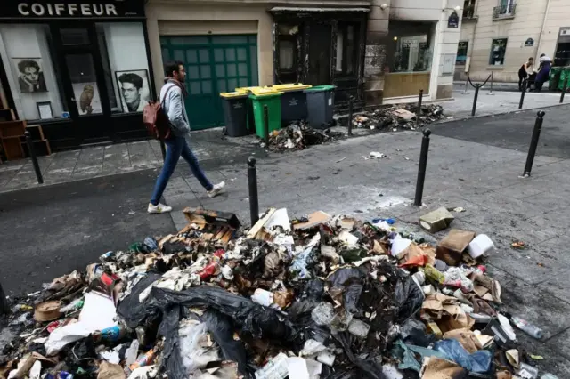 A man walks in front of piles of rubbish in Paris