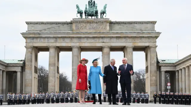 King Charles and German President Frank-Walter Steinmeier stand in front of the Brandenburg Gate alongside their wives