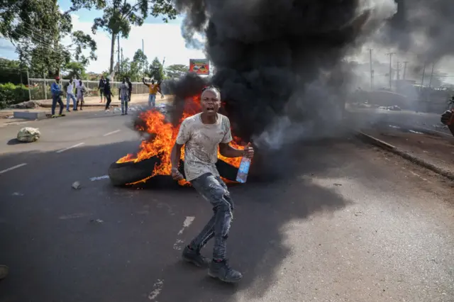 A protestor chants slogans with burning tires in the background along Ngong Road during a demonstration called by Azimio party leader Raila Odinga