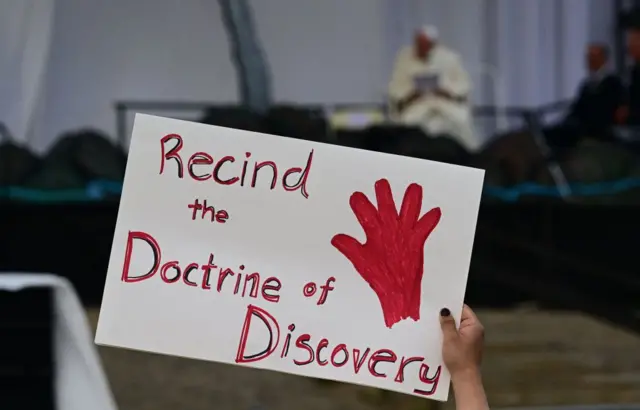 A person holds a protest sign reading "Recind the Doctrine of Discovery" as Pope Francis speaks on stage at Nakasuk Elementary School Square in Iqaluit, Nunavut, Canada, on July 29, 2022.