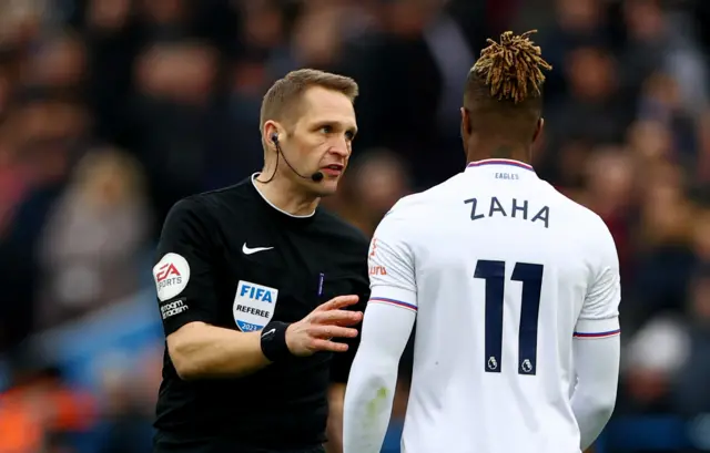 Referee Craig Pawson speaks with Crystal Palace forward Wilfried Zaha