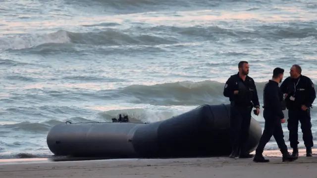 French policemen stand beside a dinghy lying on the beach near Calais