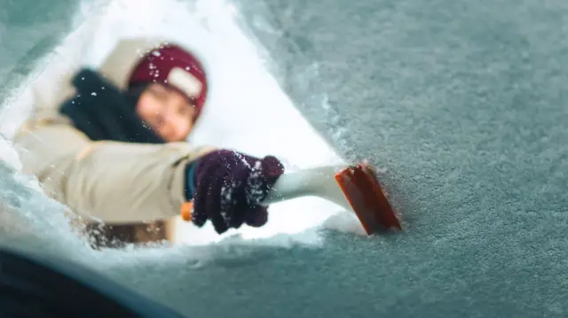 Woman cleans windshield with ice scraper