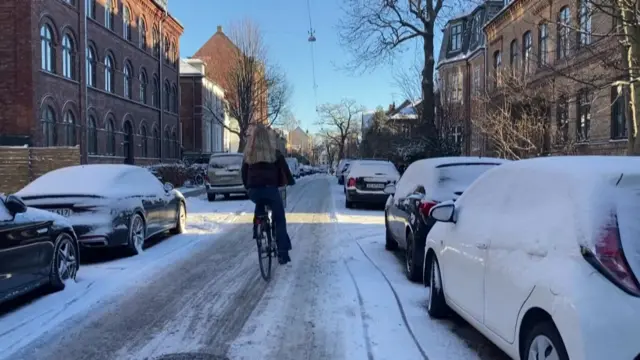 Woman rides bike on snowy street in Copenhagen, Denmark