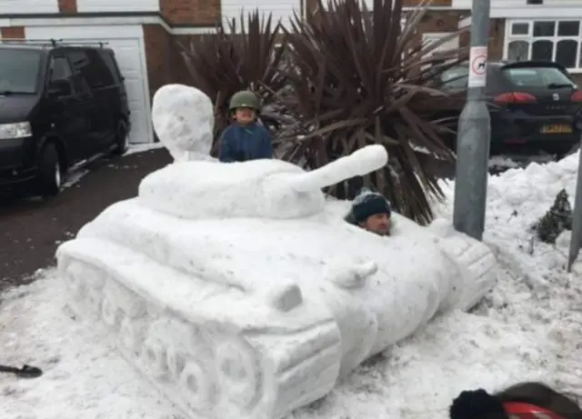 Andy Rawbone and his child pose with a tank sculpture made out of snow