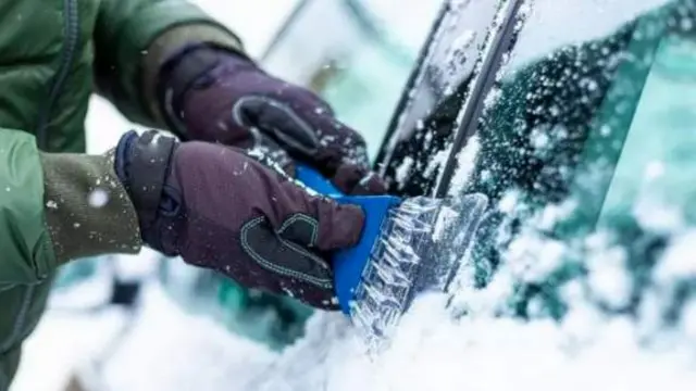 A person scraping ice off a car