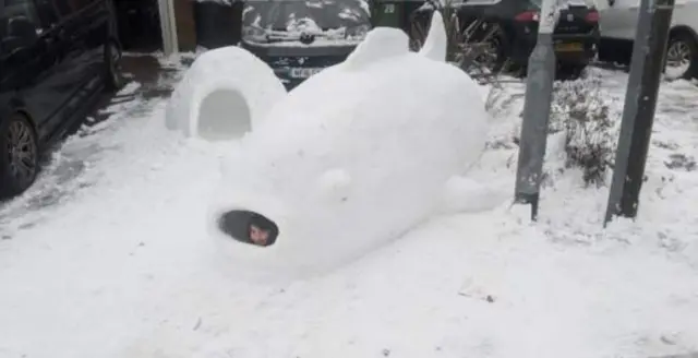 A child pictured inside a large fish sculpture made out of snow