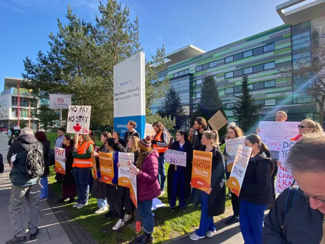 Doctors in front of a hospital holding signs