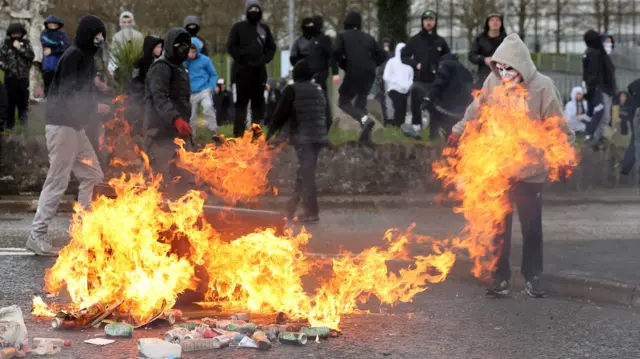 Youths throw petrol bombs at bin to block a street in the Creggan area of Londonderry on Easter Monday