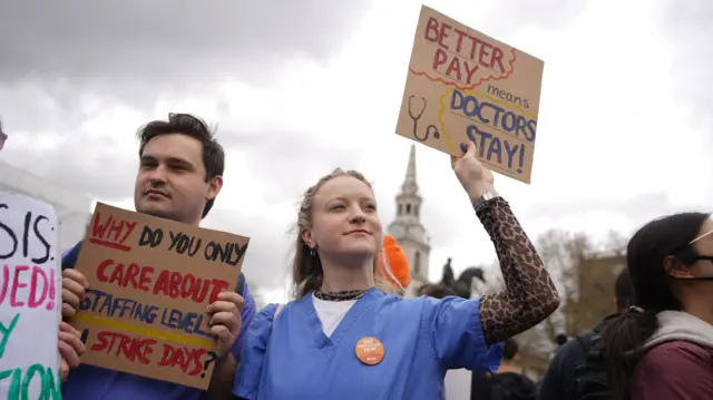 A woman holds a sign saying "better pay means doctors stay"