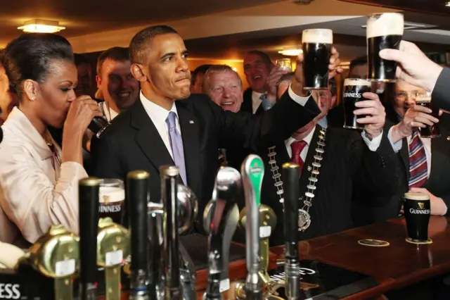 Barack and Michelle Obama drinking Guinness in a pub with others