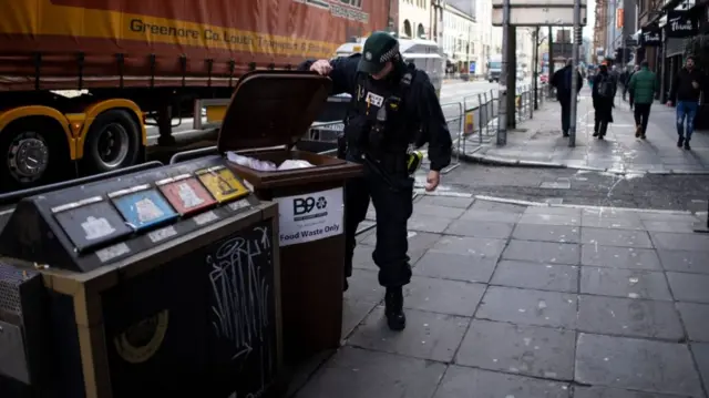 A police officer checks and moves the bins away from roads near Grand Central Hotel