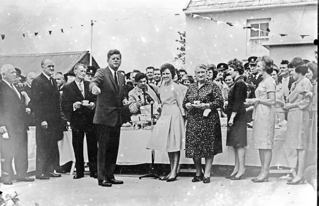 A black and white photo of John F Kennedy in an Irish street with locals