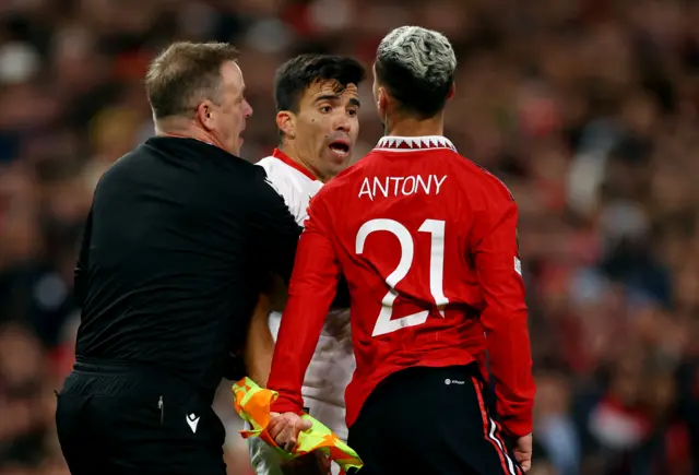 Manchester United's Antony clashes with Sevilla's Marcos Acuna as assistant referee Marco Achmuller intervenes