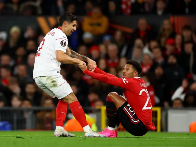 Sevilla's Gonzalo Montiel helps up Manchester United's Jadon Sancho