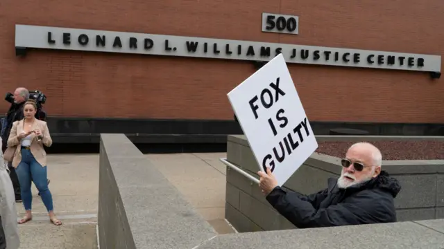 A man holds a placard saying 'Fox is guilty' outside the courthouse