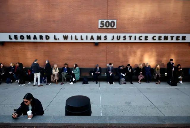 People wait against a wall at the courthouse