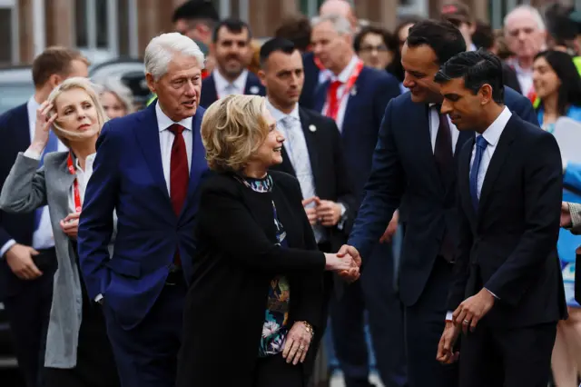 Hillary Clinton and Leo Varadkar shake hands as they walk past Queen's University with Bill Clinton and Rishi Sunak