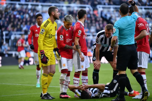 Fabian Schar of Newcastle United lies injured but is helped by Nick Pope, goalkeeper of Newcastle United Bruno Fernandes of Manchester United and Stuart Attwell, Referee