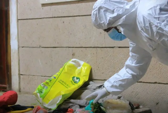 Investigator = in protective mask and overalls, examining abandoned clothes outside the school