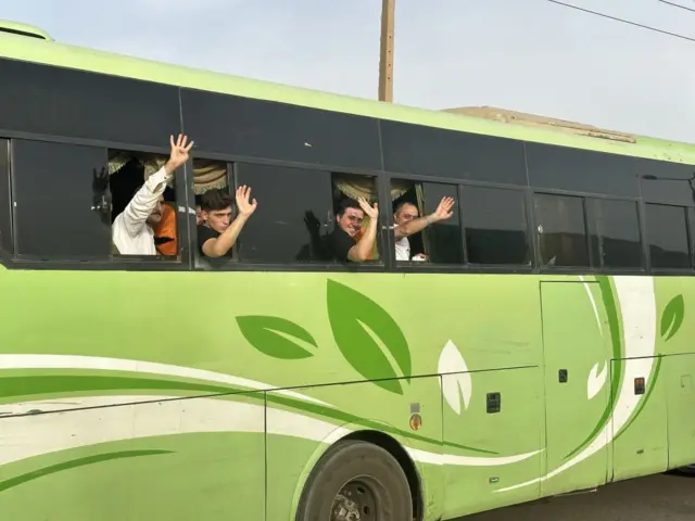 A group of people wave from the side of a bus