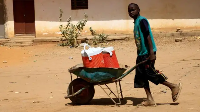 Boy with wheelbarrow of water containers in Khartoum - 23 April