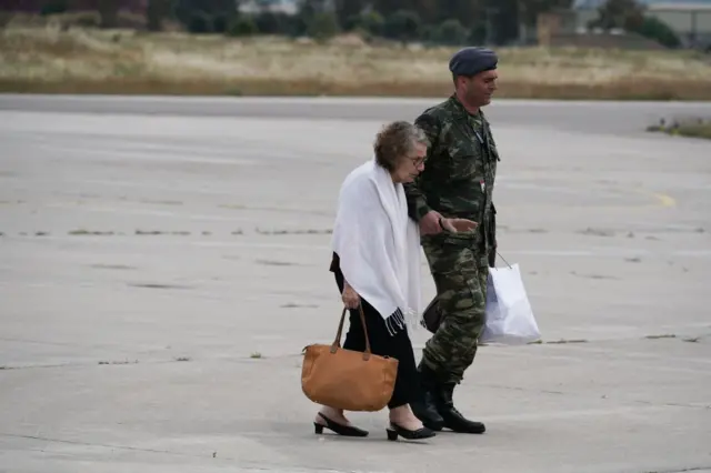 An elder Greek citizen, rescued from Sudan, is walked by a soldier on the airstrip after disembarking a Hellenic Air Force C-27 aircraft, from Aswan, Egypt, at the military airport of Elefsina, on 25 April 2023