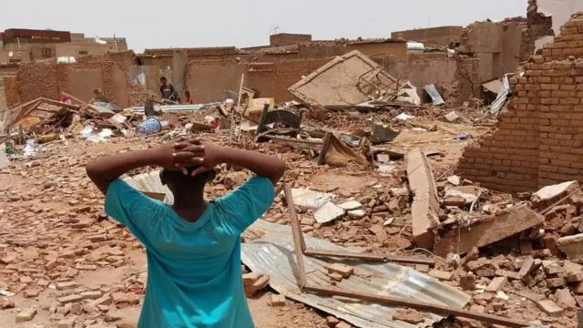 A child stands in front of damaged buildings following fighting in Sudan