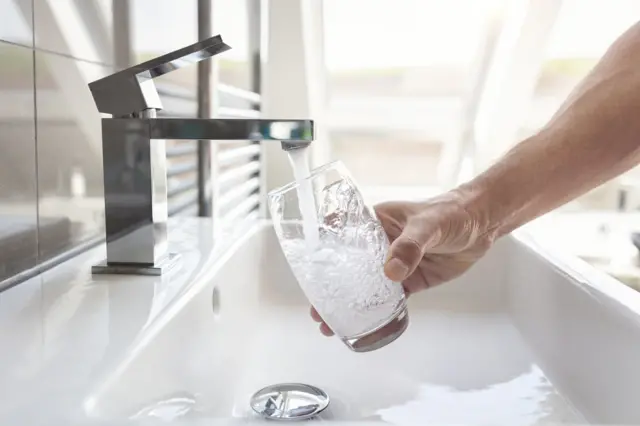 A man filling glass of water from tap