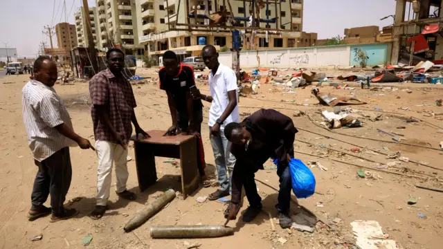 People look at artillery shells on the ground near damaged buildings at the central market in Khartoum North