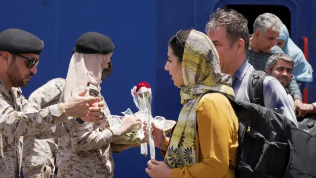 A woman is greeted with a rose by men in military uniform after disembarking a boat in Saudi Arabia