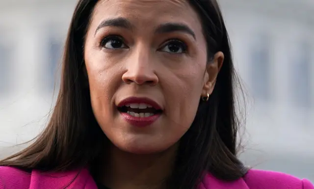 Democratic Congresswoman Alexandria Ocasio-Cortez seen during a speech. She is wearing a pink coat.