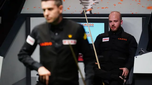 Luca Brecel watches Mark Selby prepare to play a shot