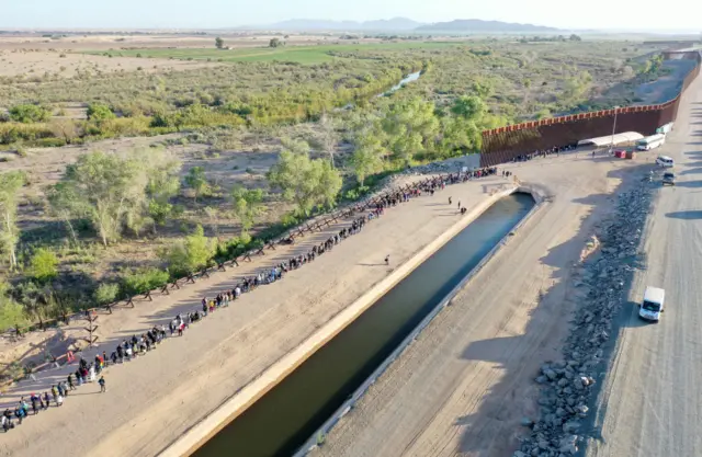 In an aerial view, immigrants seeking asylum in the United States wait in line near the border fence to be processed by US Border Patrol agents after crossing into Arizona from Mexico