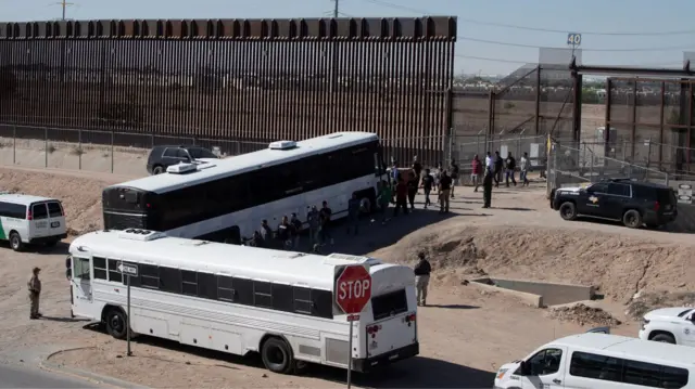 Migrants are escorted past a US border gate and to US Customs and Border Protection buses