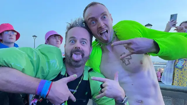 Two friends wearing green pose for a photo outside eurovision