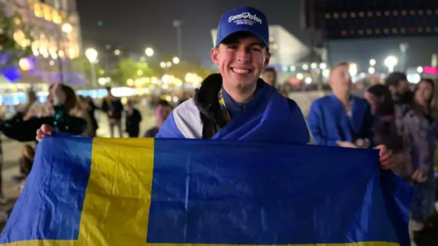 Alastair smiles holding a Swedish flag