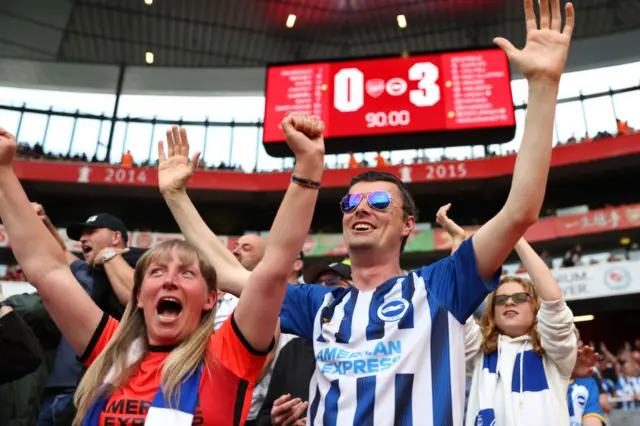 Brighton fans celebrate after the team's 3-0 win at Arsenal, with the scoreboard in the background