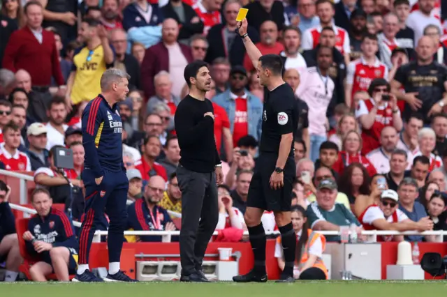 Referee Andy Madley shows a yellow card to Arsenal manager Mikel Arteta during their game against Brighton