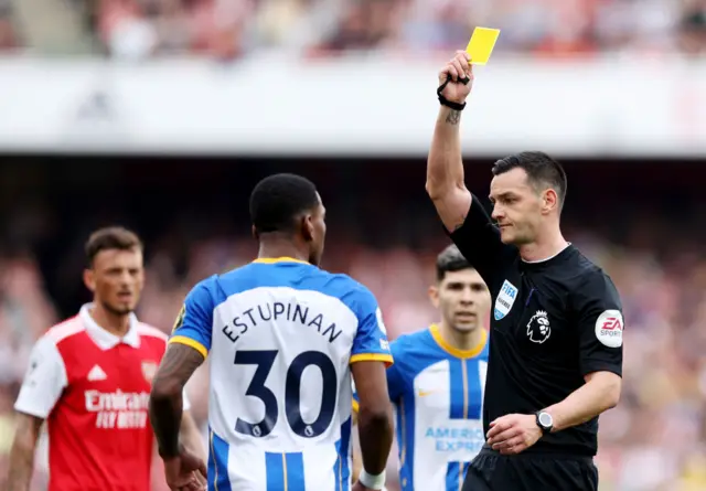 Referee Andy Madley shows a yellow card to Pervis Estupinan of Brighton during their game against Arsenal