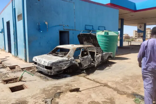 A man walks toward a charred car in a looted petrol station in southern Khartoum, on May 6, 2023