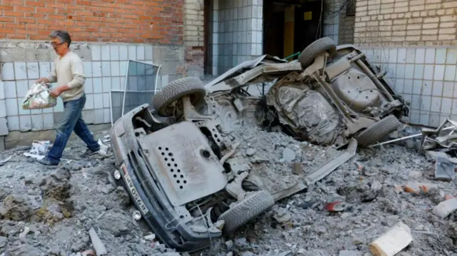 A resident walks past an overturned car in Yasynuvata, Donetsk region