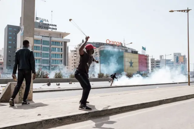 A protester uses a slingshot to hurl a stone to police forces during a demonstration on a highway in Dakar on March 30, 2023.