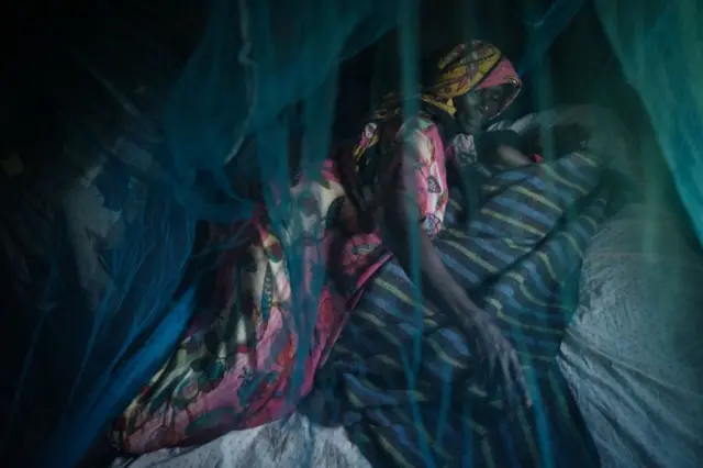 Ruth Kavere, 65, demonstrates to use a mosquito net with her granddaughter Faith, 3.