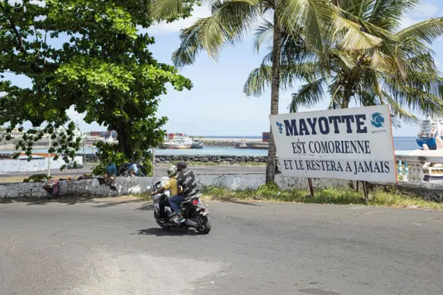 A motorcycle rides past a sign which reads " Mayotte is Comoran and will remain so forever" in Moroni, on the Ngazidja island in the Comoros Archipelago on May 6, 2023.